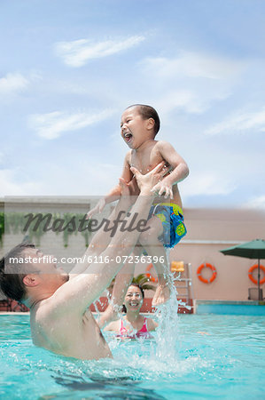 Smiling family playing in the pool, father lifting his son out of the water