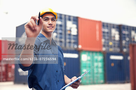 Smiling young engineer in protective work wear in a shipping yard examining cargo