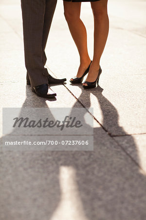 Close-up of young couples legs and feet with shadows, wearing dress shoes and standing on sidewalk, Canada