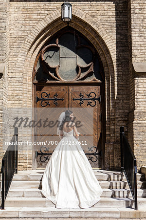 Backview of bride in wedding gown, standing in front of church door on Wedding Day, Canada