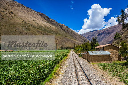 Train rails next to rural homes and farmland on scenic journey through the Sacred Valley of the Incas in the Andes mountains, Peru