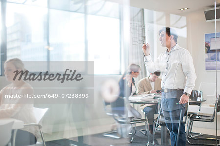 Man writing on glass wall, colleagues in background