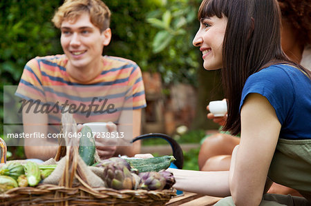 Friends sitting in garden with basket of fresh vegetables
