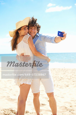 Couple self photographing with mobile phone on beach