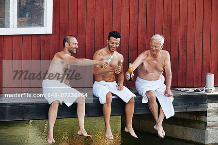 Three men sharing a beer outside sauna Three men sharing a beer outside sauna