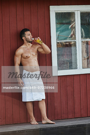 Young man drinking a beer outside sauna