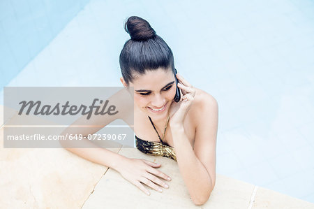 Young woman in swimming pool using mobile phone