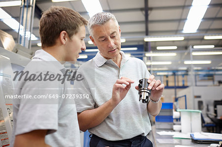 Manager and working looking at component in engineering factory