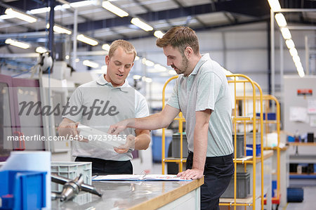 Workers discussing component in engineering factory Workers discussing component in engineering factory