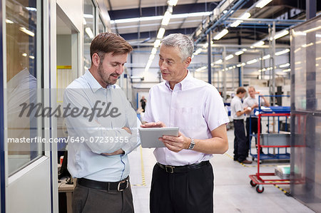 Manager and worker looking at digital tablet in engineering factory Manager and worker looking at digital tablet in engineering factory