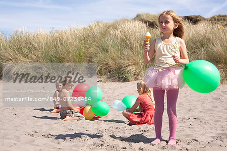 Girl holding balloon eating ice cream on beach, Wales, UK