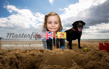Young girl on with sandcastle on beach, Walberswick, Suffolk, England, UK