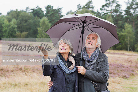 Senior couple under umbrella checking for rain