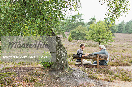 Senior man and mid adult man sitting on bench Senior man and mid adult man sitting on bench