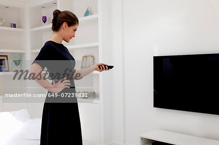 Young woman wearing black dress switching on tv