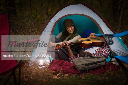 Mature couple sitting in tent, playing guitar