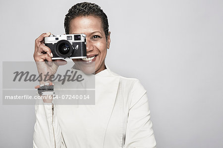 Studio portrait of happy mature woman holding up camera