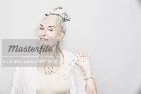 Studio portrait of sophisticated senior woman holding beads