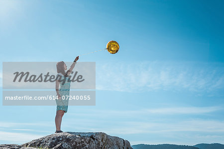 Mature woman standing on rock with golden balloon