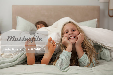 Portrait of girl lying on bed with mothers feet