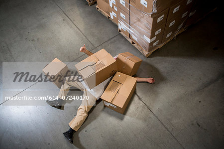 Man lying on floor covered by cardboard boxes in warehouse