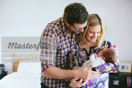 Mom and Dad holding newborn, baby boy standing in bedroom, USA