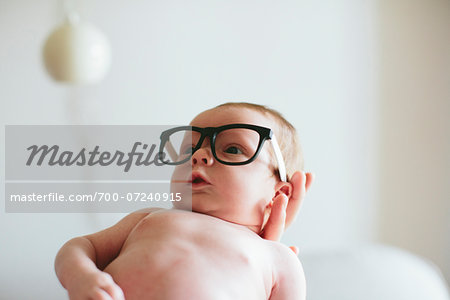 Three week old baby boy wearing glasses and being held in mother's hand inside home, USA