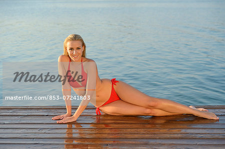 Young blond woman in bikini on a jetty at a lake, Styria, Austria