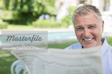 Senior man reading newspaper at poolside