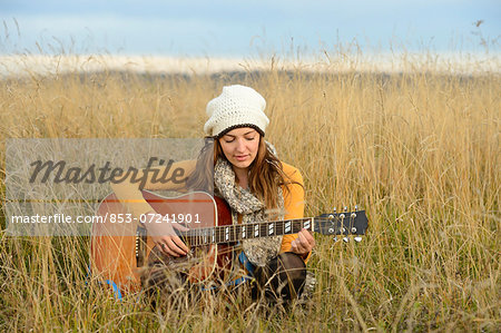 Young woman playing guitar in field