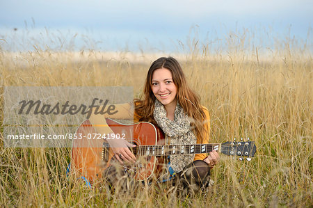 Smiling young woman playing guitar in field