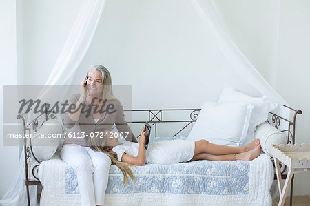 Grandmother and granddaughter with digital tablet and cell phone on daybed