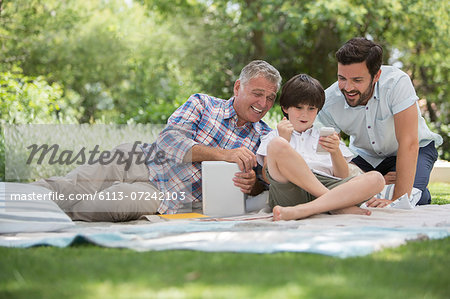 Multi-generation men with cell phone on blanket in grass