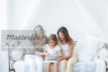 Multi-generation women using digital tablet on daybed