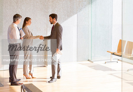 Business people shaking hands in sunny office lobby