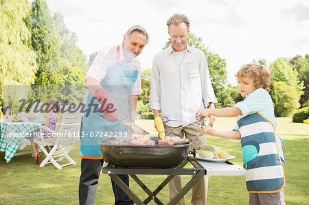 Men grilling meat on barbecue in backyard