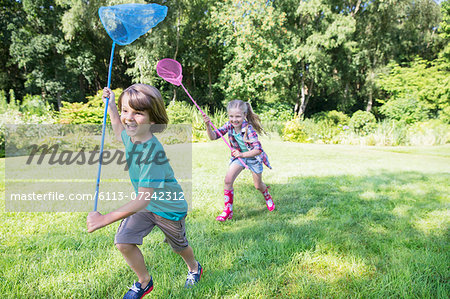 Boy and girl running with butterfly nets in grass