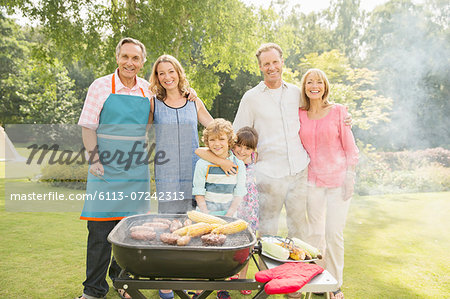 Multi-generation family standing at barbecue in backyard
