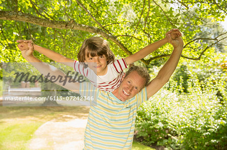 Father piggybacking son under tree