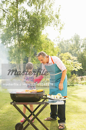 Grandfather and granddaughter grilling at barbecue in backyard