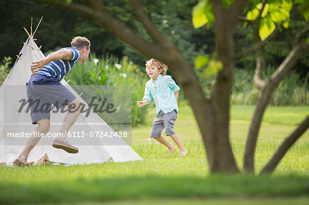 Father chasing son around teepee in backyard