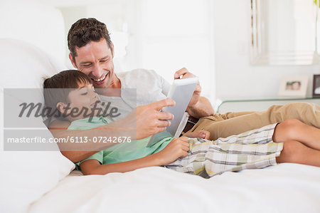 Father and son using digital tablet on bed Father and son using digital tablet on bed