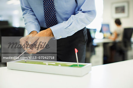 Businessman playing with toy golf set in office