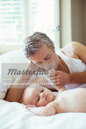 Father kissing baby's hand on bed