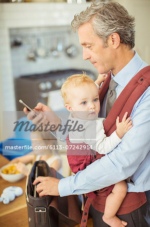 Father holding baby and checking cell phone