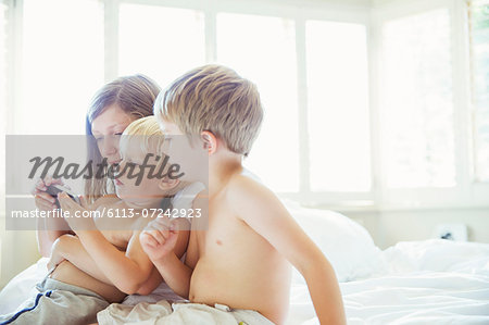 Children using cell phone on bed
