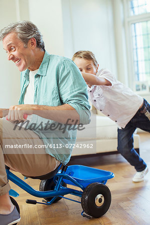 Boy pushing father on tricycle indoors Boy pushing father on tricycle indoors