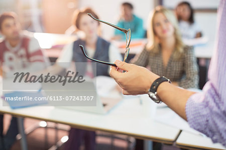 Professor gesturing with eyeglasses in classroom