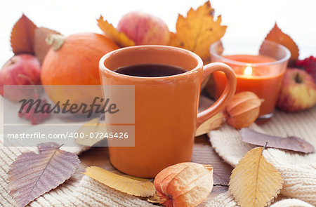 Orange coffee cup on the autumn fall leaves and candle with fruits on the background