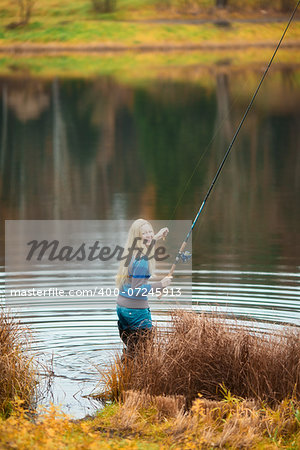 beautiful blond girl fishing in pond at autumn